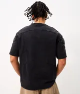 Remera boxy de algodón color negro con efecto desteñido, cuello redondo, mangas cortas y hombreras estructuradas con recortes y pespuntes.