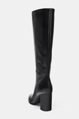 Bota alta de piel color negro, con caña alta, detalles de pespuntes verticales y tacón alto en bloque.