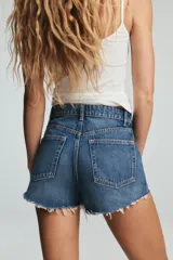 Short de jean negro desgastado, tiro alto, con roturas pronunciadas y terminación deshilachada en el bajo. Presenta cinco bolsillos y cierre frontal con botón metálico.