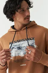 Canguro de felpa modelo Handel, color tostado, con capucha ajustable con cordones oscuros, bolsillo frontal tipo canguro y estampa gráfica inspirada en la Creación de Adán con la leyenda "Renaissance" y branding de Mistral.