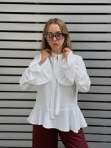 Blusa blanca de textura arrugada, con escote en V y lazos para anudar. Presenta mangas largas con puños acampanados y un diseño con volado en el ruedo.
