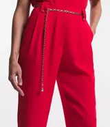 Pantalón zanahoria rojo de crepé con cintura alta, trabillas, pliegues, bolsillos y cinturón de cadena metalizada.
