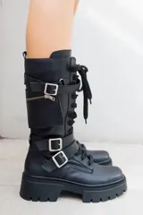 Borcegos de cuero negros, con cordones, cierre lateral y hebillas con correas ajustables. Poseen una caña de 28,5 cm de alto y una base de 4,5 cm.