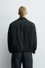 Cazadora de corte relajado confeccionada en tejido con estructura de espiga. Presenta cuello solapa, cierre frontal con cremallera, bolsillos de vivo en la cadera y bajo con pliegues en delantero y espalda.