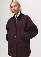 Parka color bordó, de corte recto, con cierre frontal de cremallera y botones a presión. Presenta cuello camisero de pana, bolsillos frontales de parche con solapa y mangas largas con puños ajustables. Incluye forro interior.