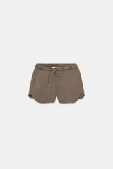 Shorts de mujer color marrón topo, de tiro medio, con cintura elástica ajustable mediante cordón y bajo con aberturas laterales redondeadas. Presenta una textura acanalada o de punto waffle.