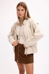 Campera de gamuza color beige con diseño de calados florales en hombros y espalda, cierre frontal y cuello camisero. Presenta un corte relajado y textura suave.