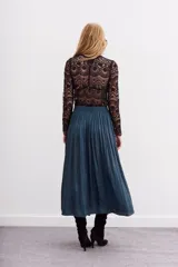 Falda larga de poliéster color azul petróleo, con cintura elastizada tipo nido de abeja, lazos de ajuste con terminales metálicas y tajo lateral.