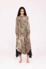 Túnica larga de manga larga, con cuello camisero y botones frontales. Presenta un estampado floral en tonos tierra y beige, con un forro o capa interna de tela negra asomando en el ruedo irregular.