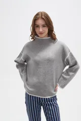 Polera de tejido suave en color gris melange, con cuello alto y detalles de vivos en color blanco en el cuello, puños y ruedo. Presenta un diseño holgado con mangas largas de caída relajada.