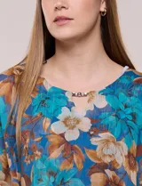 Blusa de gasa semitransparente con hilos de lúrex, diseño estampado floral en tonos blanco, gris y negro, silueta holgada tipo capa y escote redondo con detalle metálico.