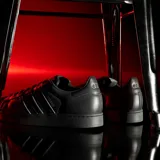 Championes Adidas modelo Superstar, color negro con las icónicas tres tiras laterales en acabado iridiscente y puntera de goma clásica.