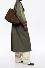 Bolso tipo shopper de Bimba y Lola, color marrón, confeccionado en gabardina con detalles en piel. Cuenta con doble asa de hombro y cierre principal con cremallera.