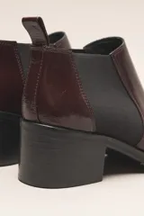 Botín chelsea de cuero vacuno color bordó con acabado charol, punta fina y elástico lateral negro. Posee un taco ancho y bajo de goma.