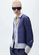 Camisa de tejido fluido con acabado satinado, diseño de rayas verticales en tonos azul marino, blanco y celeste. Presenta cuello camisero, cierre frontal con botones y mangas largas con puños abotonados.