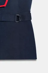 Chaleco de escote pico con solapa y manga sisa, color azul marino con vivos contrastantes en rojo y detalle de hebilla en el lateral.