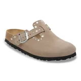 Zueco tipo Boston en color taupe, confeccionado en gamuza con detalle de remaches metálicos decorativos. Cuenta con una tira ajustable con hebilla metálica, plantilla de corcho y suela de goma negra.