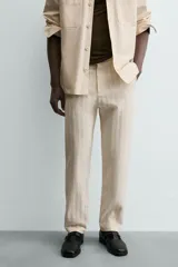 Pantalón chino de corte relajado, color beige claro, con textura de rayas verticales sutiles. Presenta cintura ajustable con cordón interior, bolsillos delanteros y bolsillos traseros de vivo.