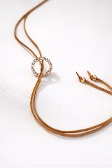 Choker marrón de gamuza con dije de doble aro entrelazado, uno liso y otro con incrustaciones de strass. Los extremos del choker tienen detalles de cuentas doradas.