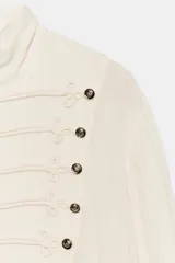 Camisa ZW Collection de viscosa color marfil, con cuello subido, manga larga terminada en puño elástico y bajo asimétrico. Presenta cierre frontal con alamares y botones en relieve.