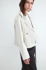 Campera estilo trench corta color beige, con solapas amplias, cierre cruzado de doble botonadura con botones oscuros y diseño holgado.