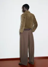 Chaqueta corta de piel de serraje color marrón, con diseño recto, cuello camisero, manga larga y cierre frontal de botones metálicos. Cuenta con dos bolsillos de parche con solapa en la parte delantera y forro interior.