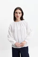 Blusa de manga larga color negro, confeccionada en 100% algodón con textura bordada. Presenta detalles de tablas en el frente y en los puños, con un corte holgado y cuello redondo con pequeña abertura.