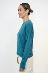 Blusa de manga larga color verde petróleo, con cuello redondo y corte relajado. Confeccionada en viscosa, presenta un diseño básico y versátil con hombros caídos.