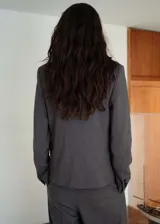 Chaqueta de corte recto estilo sastre, color gris, con cuello de solapa con muesca, cierre frontal de tres botones, bolsillos laterales de ribete y un bolsillo de ribete en el pecho. Cuenta con forro interior y mangas largas.