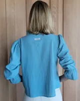 Blusa rosada de algodón con delicados bordados florales blancos, escote en V con cuello elevado y volados, y mangas largas con puños acampanados.