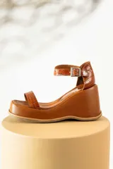 Sandalias negras de cuero sintético con plataforma y taco de cuña. Tienen dos tiras en el empeine y una tira con hebilla alrededor del tobillo.