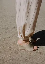 Pantalón balloon de tiro medio en color beige con estampado de rayas finas verticales oscuras. Presenta diseño abombado con bajo ajustable mediante botón.