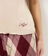 Pijama de dos piezas compuesto por una remera de manga corta en color beige con cuello redondo y un pantalón largo de corte recto con estampado de cuadros estilo argyle en tonos bordó y beige, con cintura elástica.