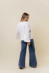 Blusa blanca de calce relajado con bordado frontal en azul de inspiración artesanal que realza el escote en V con lazo regulable. Posee mangas largas amplias con puño suave.