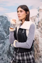 Chaleco de cuero sintético negro con interior y cuello de piel sintética blanca, cierre frontal y cintura elástica ajustada.