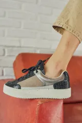 Championes urbanos con diseño de paneles en tonos verde oliva, negro y gris. Presentan una combinación de texturas que incluye cuero liso, gamuza y un panel con estampado de piel de serpiente en el talón. Cuentan con cordones negros y una suela de plataforma blanca con textura acanalada.
