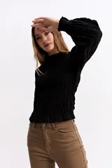 Blusa negra de algodón con textura fruncida en todo el cuerpo, cuello alto y puños con volados.