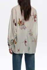 Camisa oversize de manga larga con patrón de rayas y estampado artístico multicolor, con cuello camisero, cierre frontal de botones y bolsillos en el pecho.