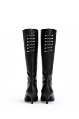 Botas altas de caña media en eco cuero negro, con taco fino de 4 cm y punta fina. Presentan un detalle decorativo de una hilera de alfileres de gancho metálicos plateados en la parte posterior de la caña.