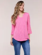 Blusa rosada con textura en relieve de motivos florales, cuello redondo con pequeña muesca y mangas tres cuartos.