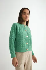 Cardigan de punto gris con diseño de ochos y trenzas, cuello redondo y cierre frontal con botones dorados grandes. Posee mangas largas con puños acanalados.