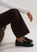 Mocasín de cuero negro con horma cuadrada, detalle de flecos y moña en el empeine, y taco bajo.