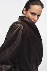Chaqueta de Zara Woman Collection confeccionada en tejido efecto piel con textura granulada. Presenta cuello solapa, manga larga y cierre frontal con cinturón ajustable anudado a la cintura. Incluye forro interior.