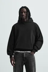 Sudadera tipo hoodie de color blanco hueso, con capucha, manga larga y bolsillo canguro frontal. Presenta un calce relajado y tejido de algodón con interior afelpado.