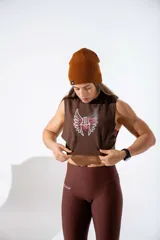 Musculosa crop top de algodón elastizado color marrón, con diseño gráfico frontal de alas y texto en tonos blanco y rosado.
