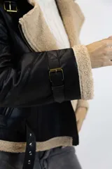 Campera oversize de efecto cuero color marrón con interior, solapas, cuello y puños de corderito sintético en tono tostado. Cuenta con detalles de tiras ajustables con hebilla en el cuello, mangas y ruedo, y cierre frontal cruzado.