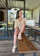 Cartera tipo bandolera de cuero color crudo, con diseño rectangular, solapa frontal con detalle de costura decorativa en el borde y correa ajustable.