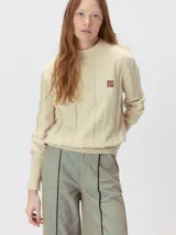 Sweater de punto color beige con cuello alto, detalles de paneles verticales texturizados y monograma bordado en el pecho.