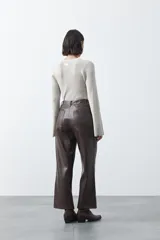 Pantalón de corte recto y pierna amplia confeccionado en símil cuero color marrón oscuro. Presenta una silueta estructurada con costuras verticales frontales que definen su diseño.