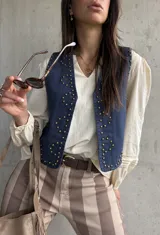Chaleco de jean oscuro con tachas doradas aplicadas en la parte frontal y escote en V.